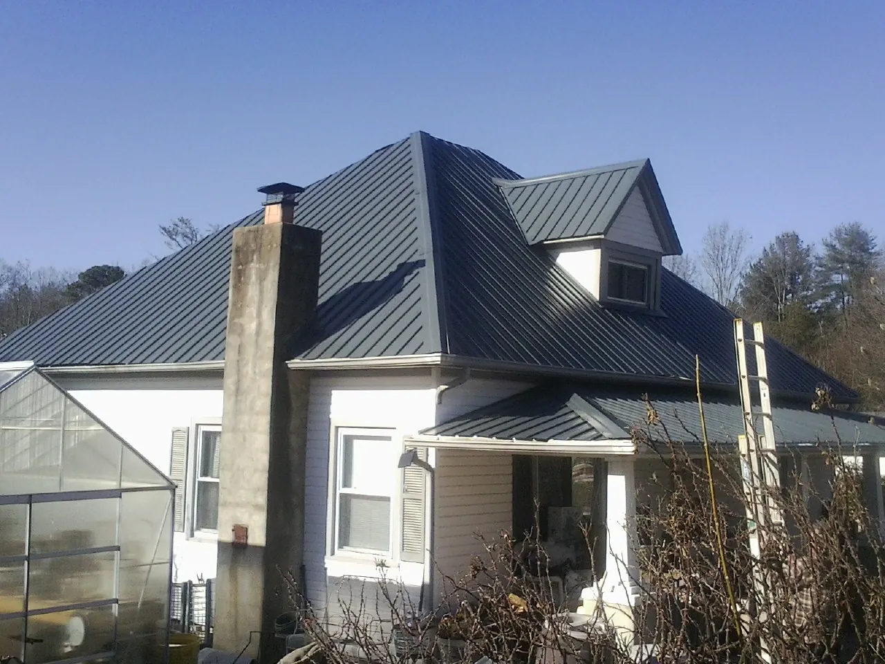 Dark blue standing seam metal roof on a white farmhouse with dormer — Slate & Tile Roof Repair by Roofing Brothers in Cowpens