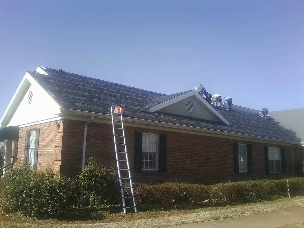 Crew tearing shingles off a brick ranch roof with a ladder set — Emergency Roof Repair work by our crew in Cowpens