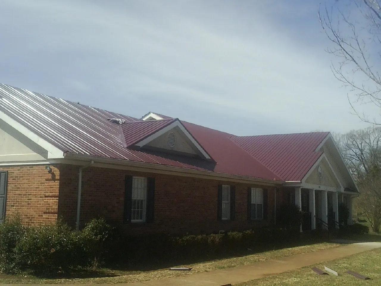 Red metal roof with gabled entries on a long brick building, from a Hail Damage Roof Repair job in Cowpens