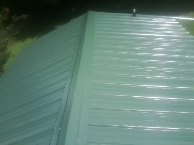 New green metal panels meeting at the ridge of a roof — Flat Roof Repair work by our crew in Cowpens