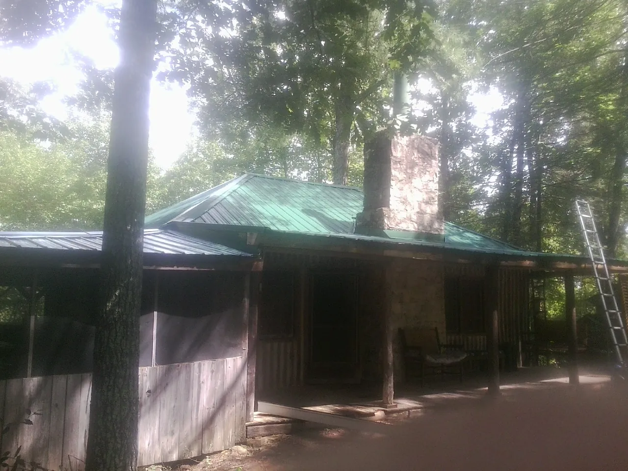 Green metal roof and stone chimney above a log cabin porch in Cowpens