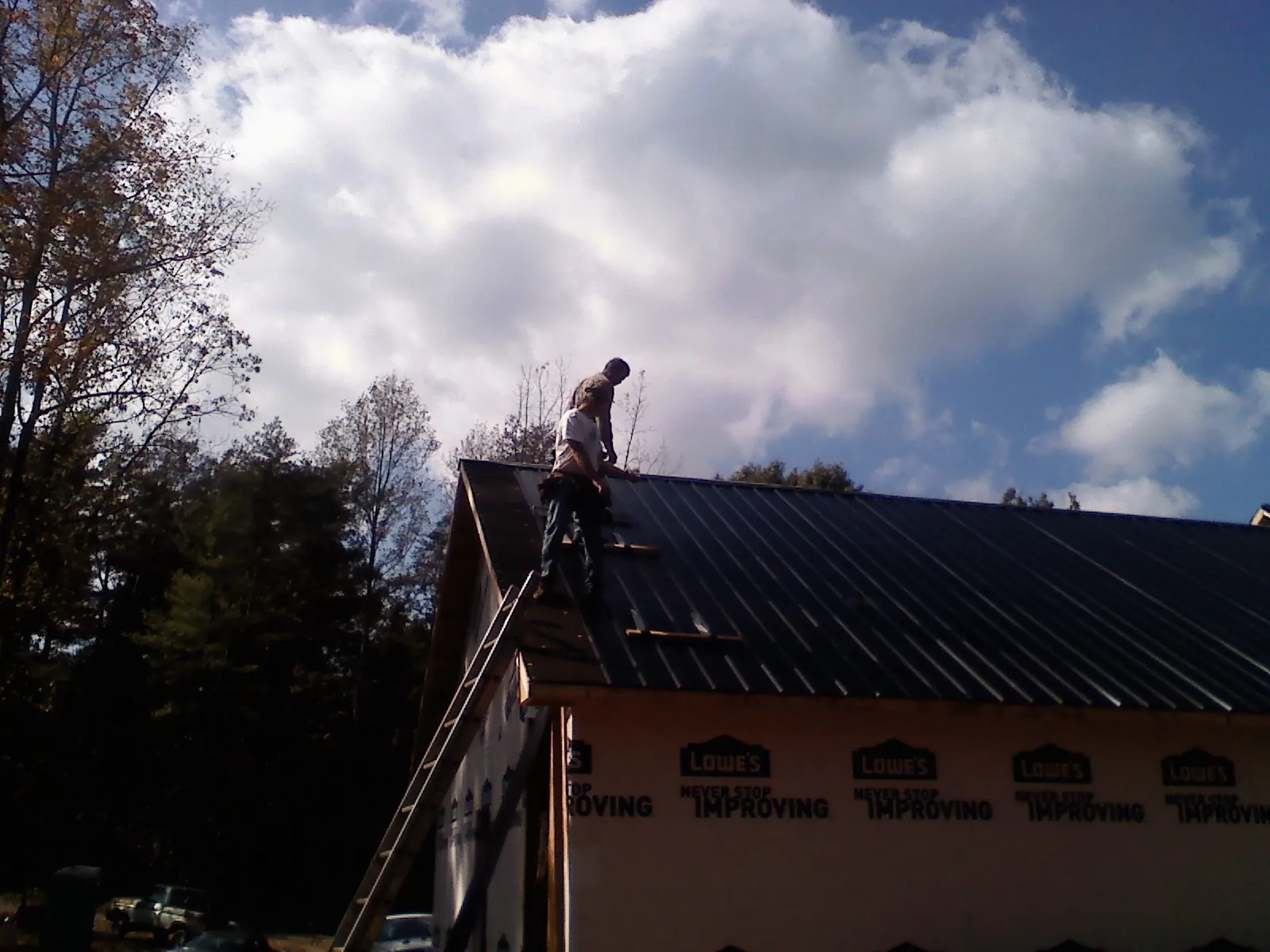 Roofer fastening dark metal panels high against a cloudy sky, from a Roof Inspection job in Cowpens