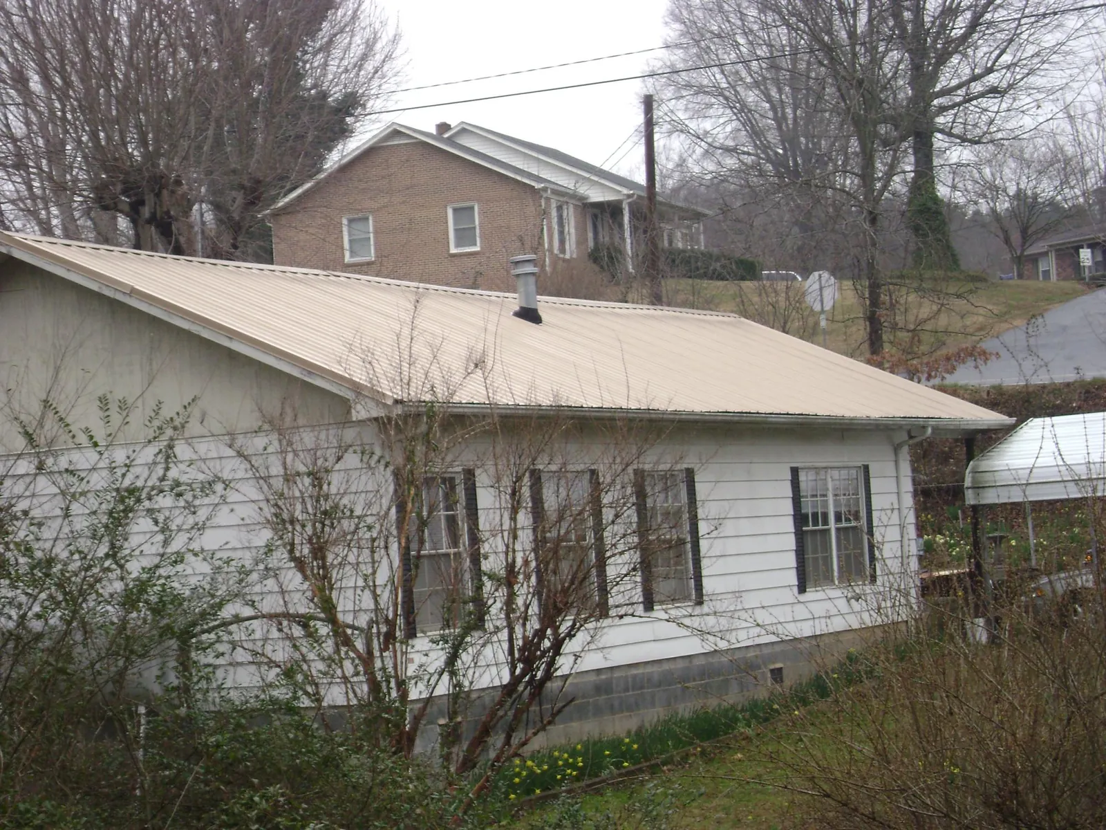 Tan metal roof on a white sided house set into a hillside — Commercial Roofing by Roofing Brothers in Cowpens